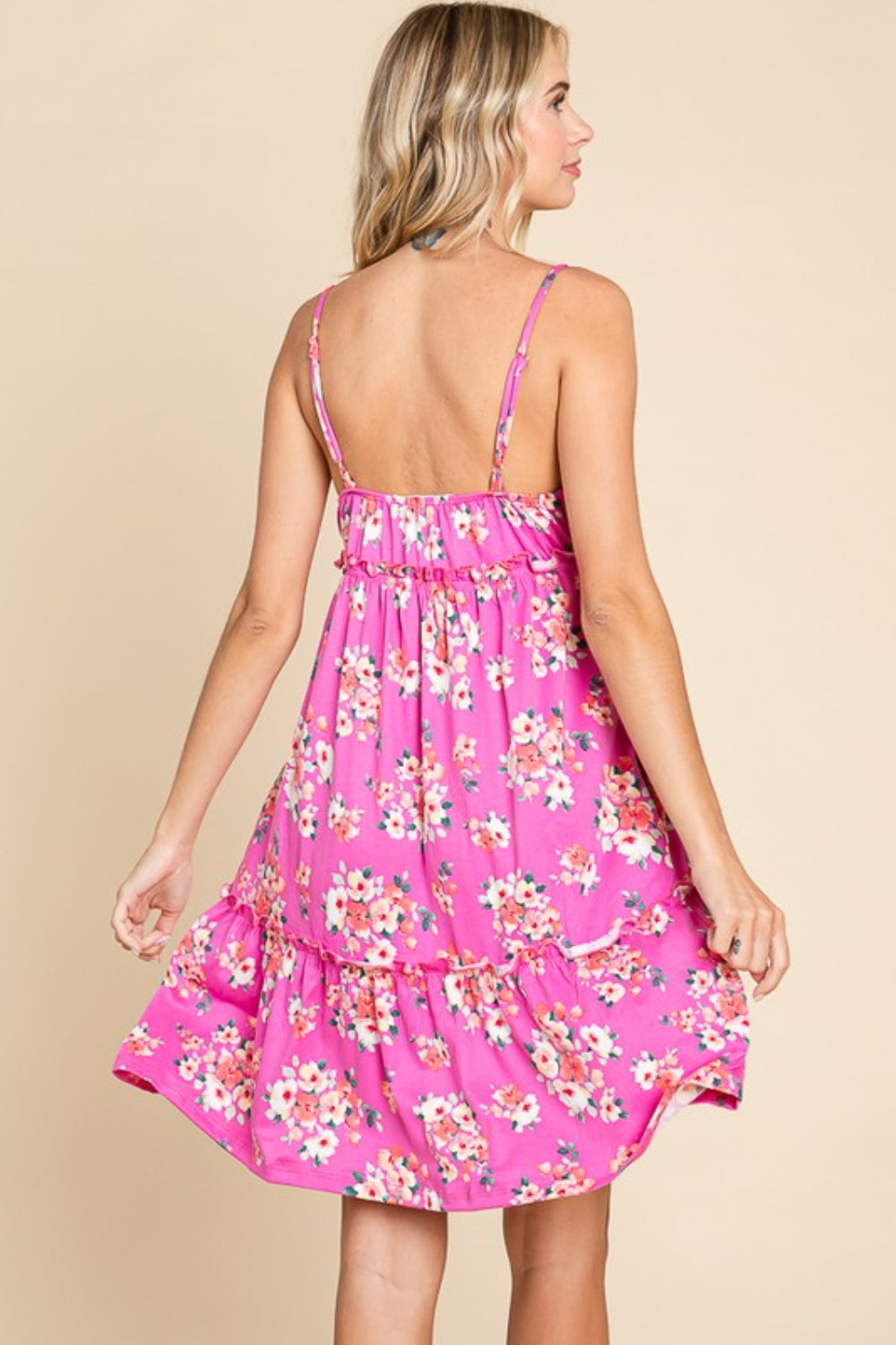 Person wearing a Culture Code Full Size Floral Ruffled Cami Dress with thin straps and a ruffled hem, standing against a beige background. This versatile option exudes feminine charm with its pink, floral design.