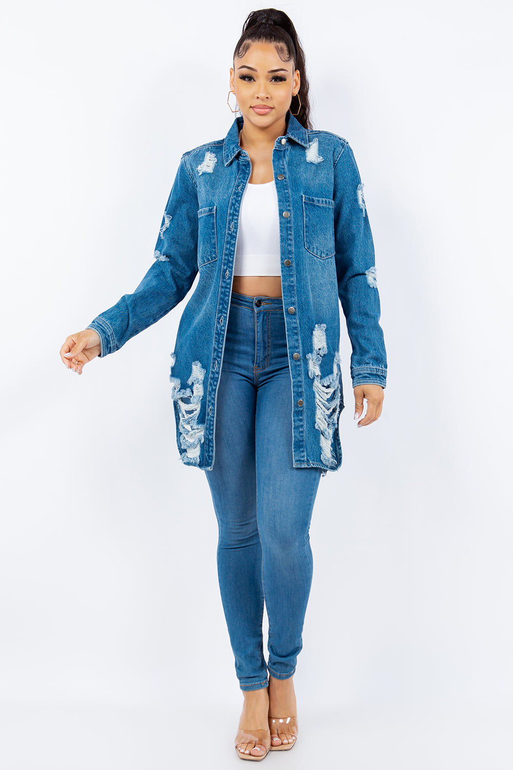 Woman wearing an American Bazi Distressed Button Up Long Sleeve Denim Jacket over a white crop top and blue jeans, standing against a plain background.