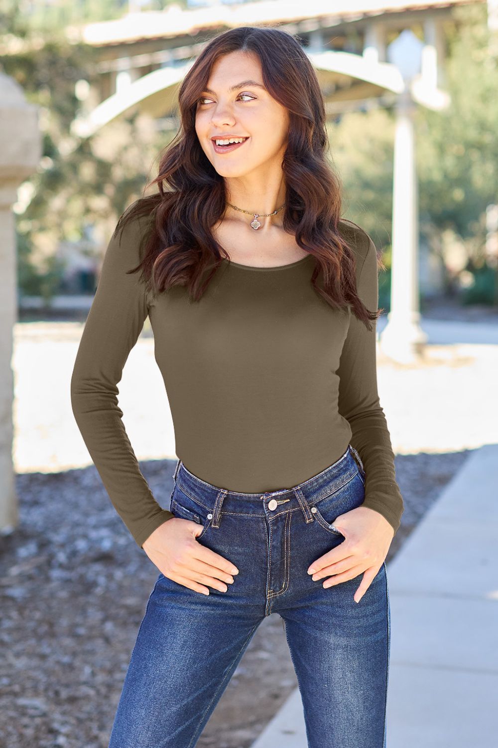 A person poses confidently in the Basic Bae Full Size Round Neck Long Sleeve Bodysuit, made from a rayon spandex blend, with one hand touching their neck and the other resting on their hip.