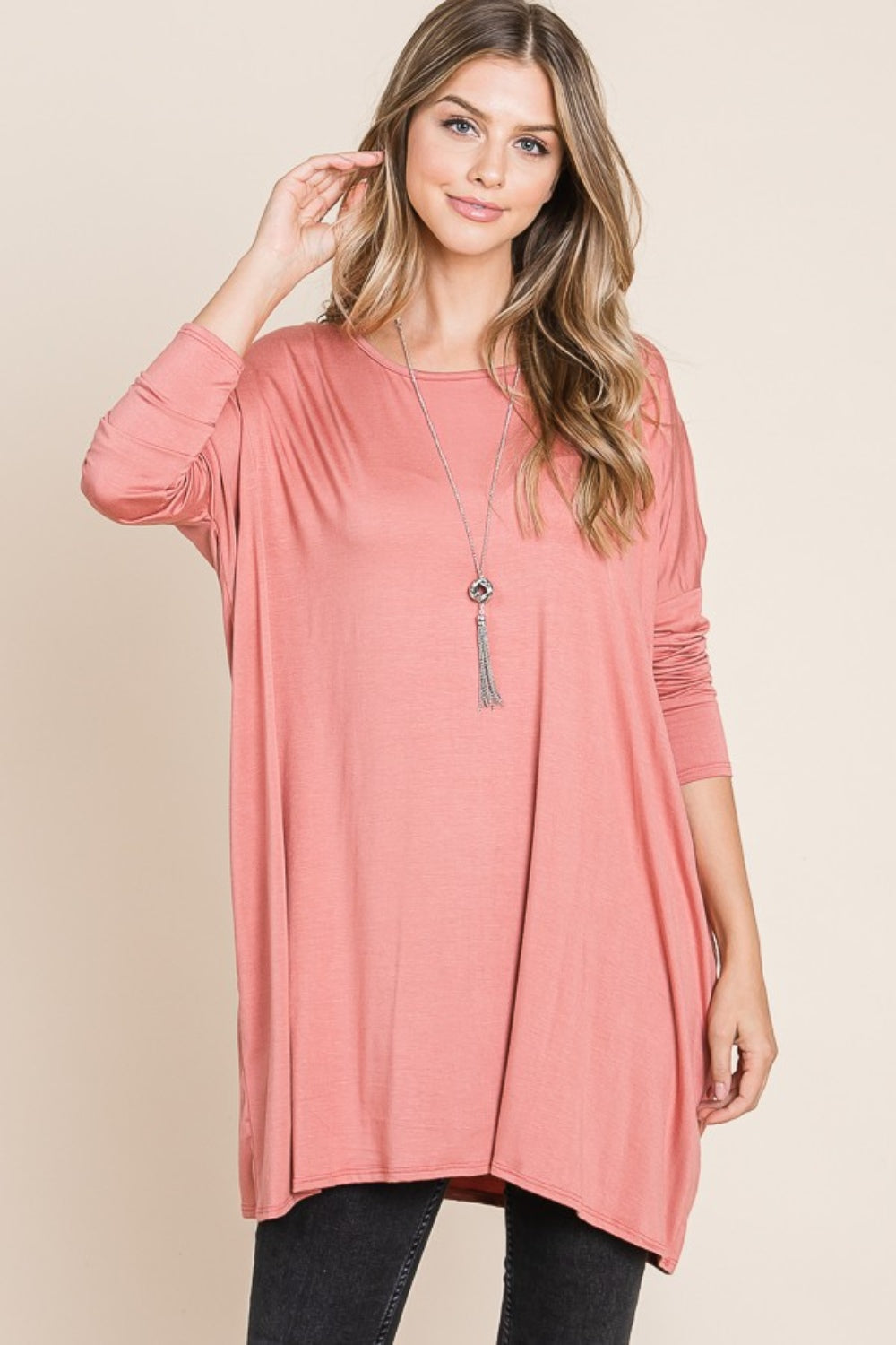 Person in a pink BOMBOM Round Neck Long Sleeve Oversized Top, wearing a long necklace, standing against a neutral background, and posing with one hand touching their hair. This oversized top is made from comfortable fabric that adds to the relaxed vibe.