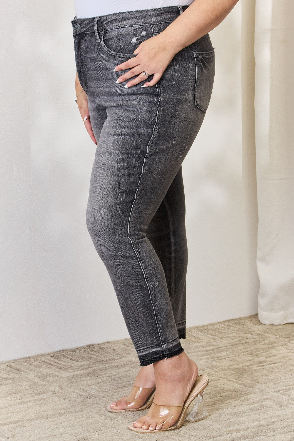 A person wearing the Judy Blue Full Size High Waist Tummy Control Release Hem Skinny Jeans paired with nude heels stands against a light background.