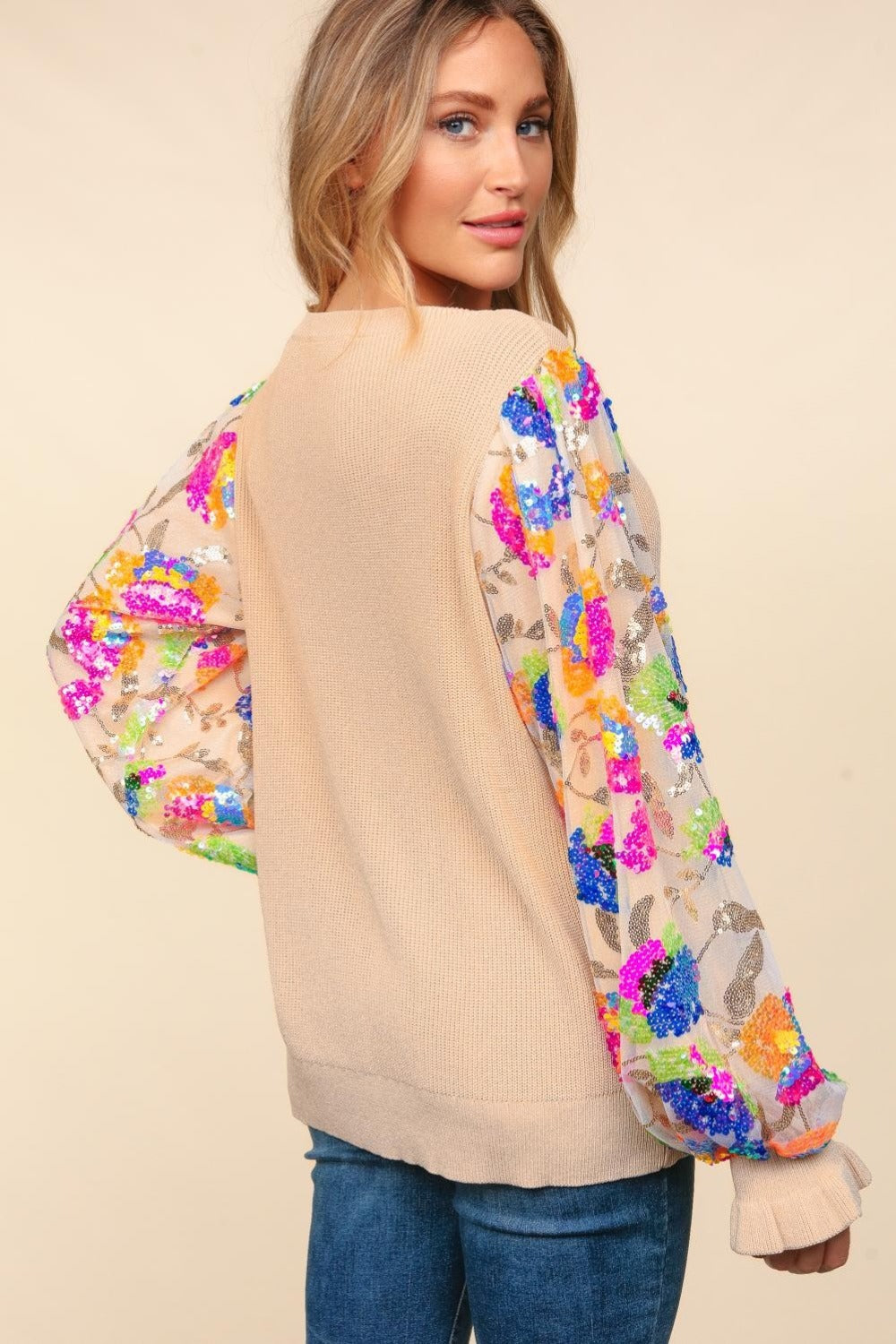 A person wearing the Haptics Floral Sequins Mesh Flounce Sleeve Sweater and blue jeans poses against a plain background.