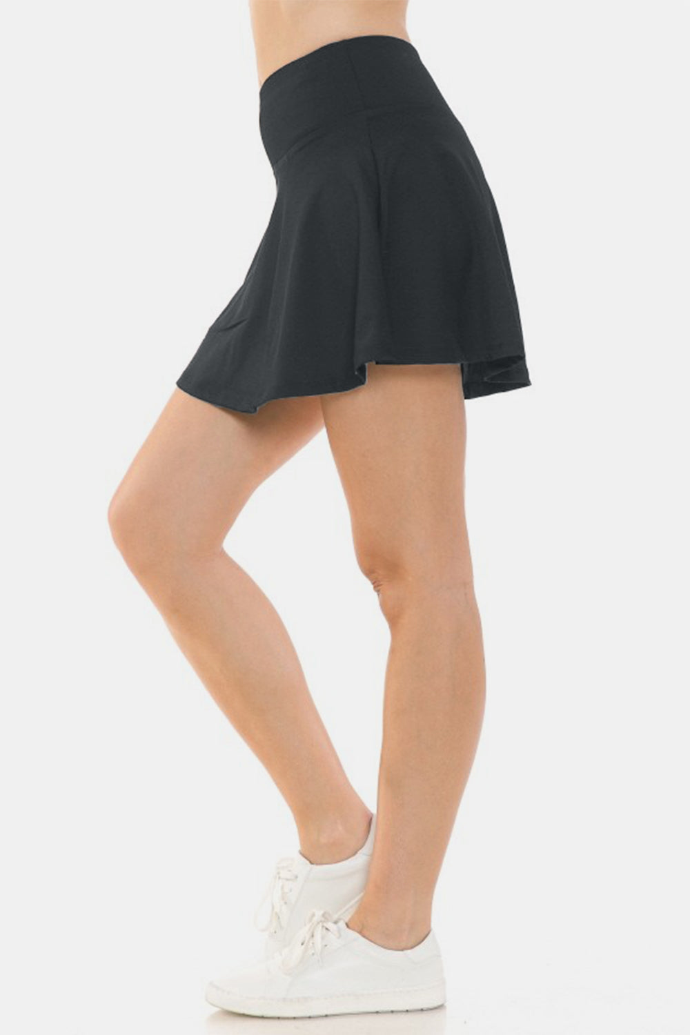 A person wearing the Leggings Depot Wide Waistband Active Skort highlights its black design with built-in shorts and a comfortable fit. The skort subtly reveals a pocket in the wide waistband, holding a white cylindrical object.