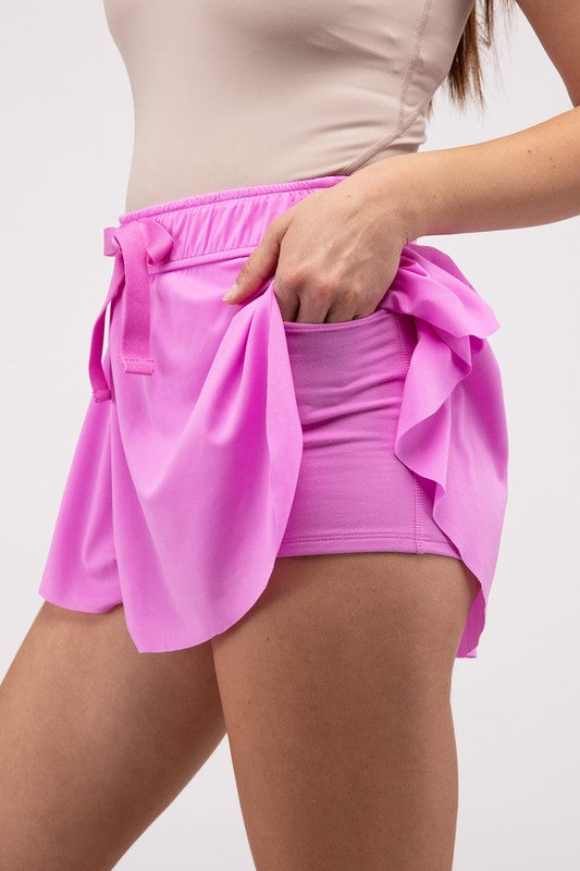 A person wearing a Ruffle Hem Tennis Skirt with Hidden Inner Pockets in vibrant pink, featuring a drawstring waist and showing only the lower torso and upper legs.