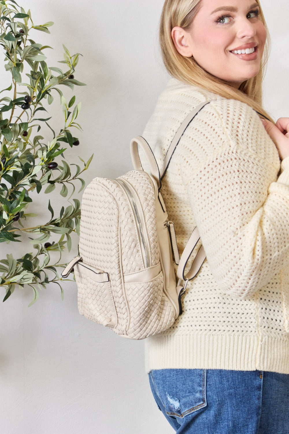 A person wearing a cream sweater and jeans is carrying the SHOMICO PU Leather Woven Backpack in brown.