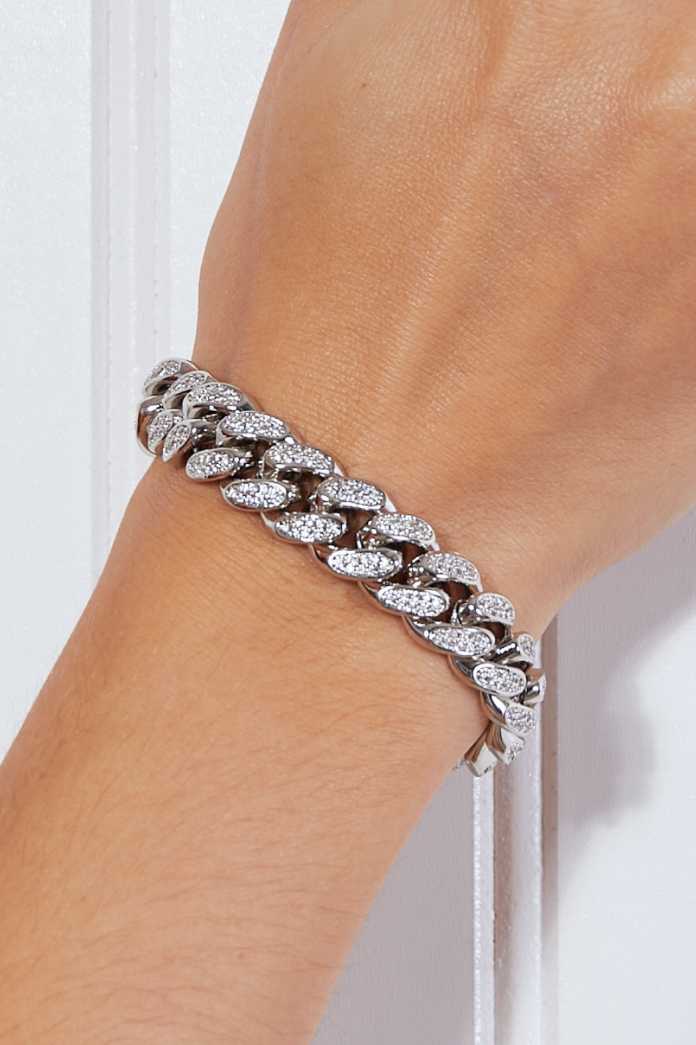 The Curb Chain Bracelet, crafted from silver and adorned with sparkling diamonds, elegantly graces the wrist against a white background.