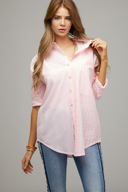 A person wearing a light pink Stripe Button Down Long Sleeve Shirt with rolled-up sleeves and jeans stands with their hands behind their head against a plain background.