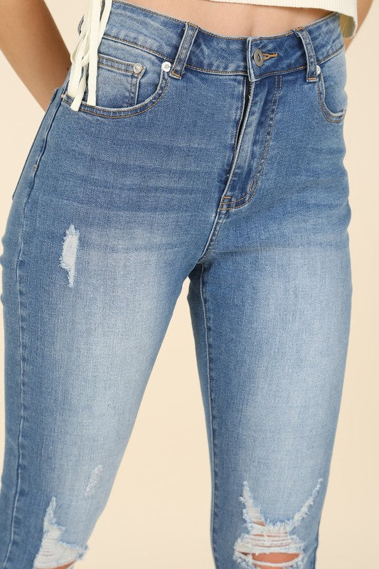 Someone wearing a sleeveless top and Dark Wash Distressed Skinny Jeans is kneeling on a white chair against a beige background.