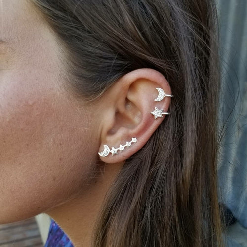 Close-up of a woman's ear with multiple piercings, showcasing the Moon & Star Earring and Cuff Set adorned with moon and star-shaped designs plus elegant crystal ear cuffs.