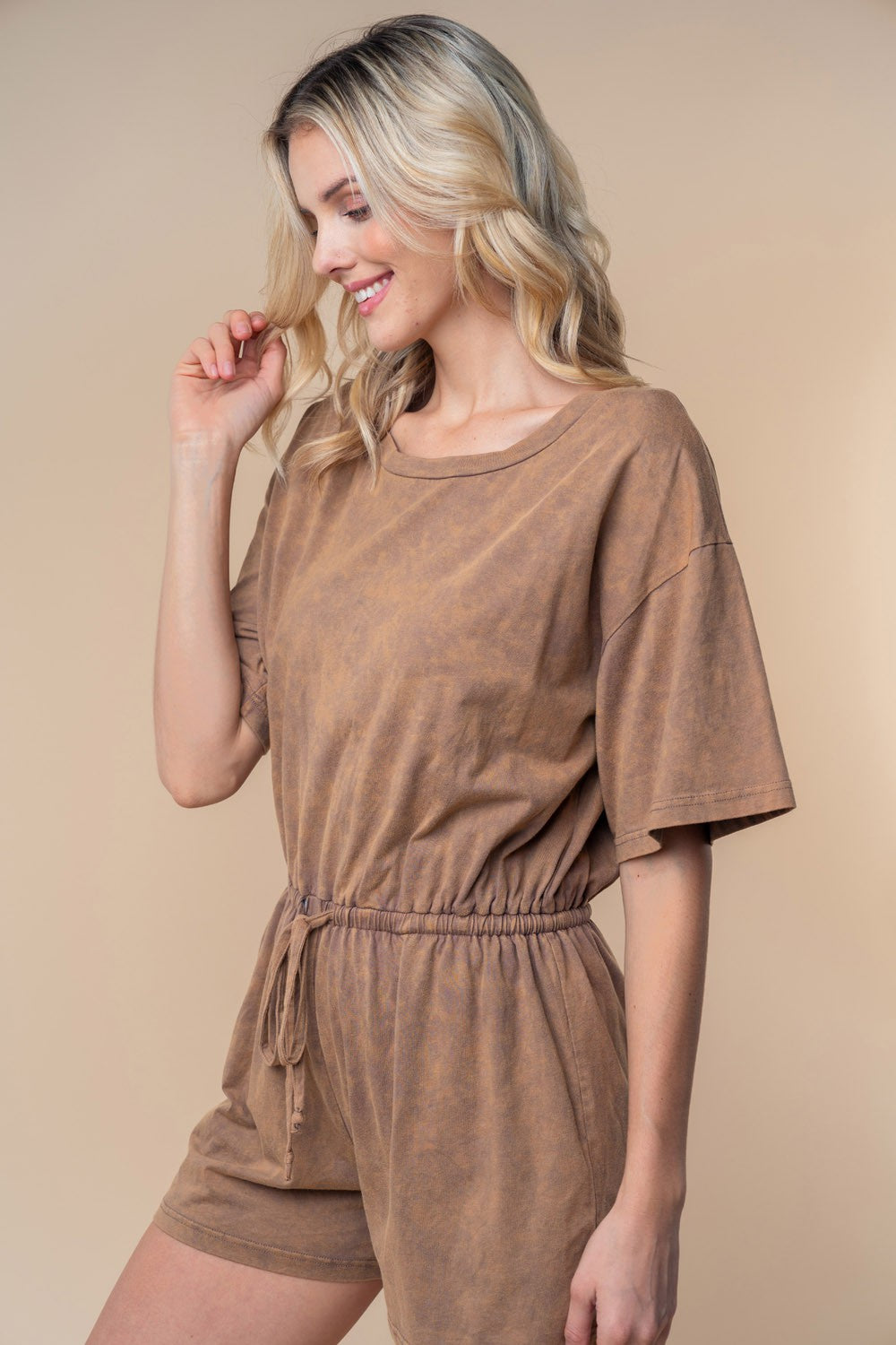 A person wearing the White Birch Full Size Short Sleeve Drawstring Romper stands against a beige background, looking slightly to the side. Perfect for your summer wardrobe, this stylish ensemble is both comfortable and chic in a cotton knit texture.