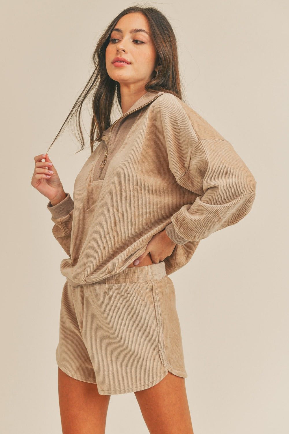 A woman stands confidently, wearing the MABLE Corduroy Half Zip Top and Shorts Set in a matching beige color, with her hands on her hips against a neutral background, effortlessly exuding retro charm.