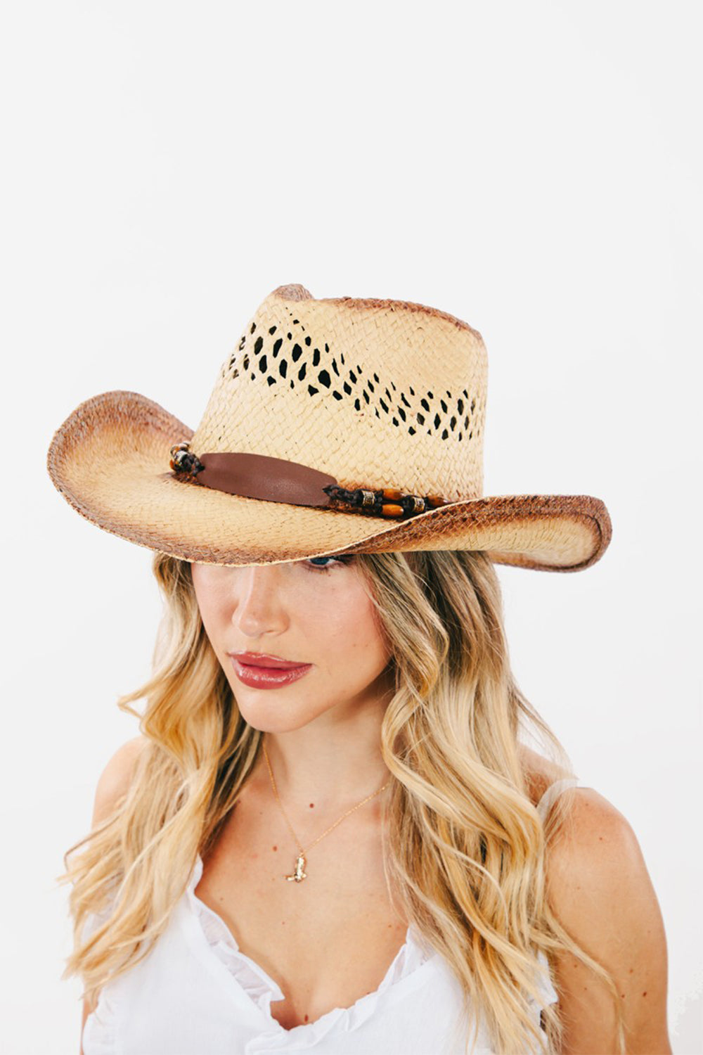 The Fame Cutout Wide Brim Straw Hat is a chic accessory featuring a brown leather band with decorative beads. Its fashionable cutout detailing and patterned, vented crown make it both stylish and functional.