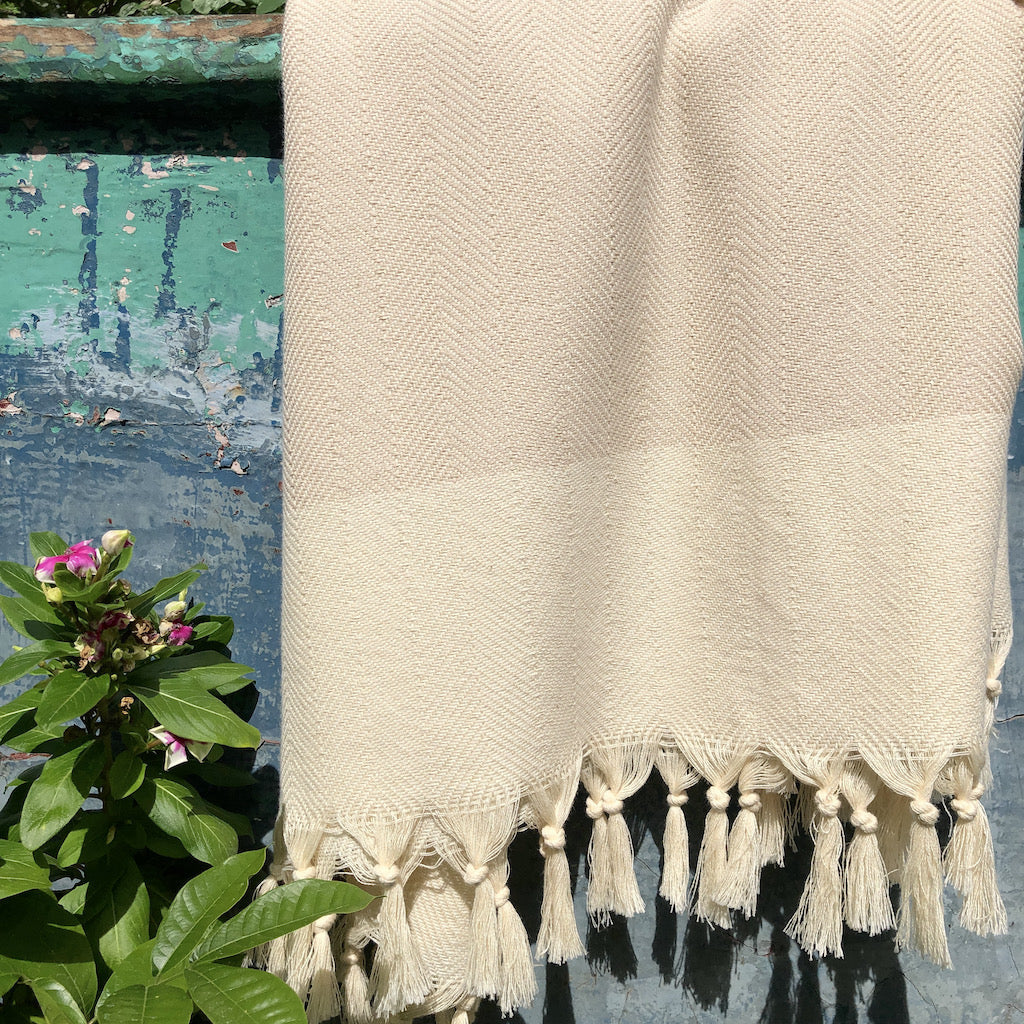 This Herringbone Turkish Towel, crafted from 100% Turkish cotton and adorned with a black and white chevron pattern, features hand-knotted fringes elegantly laid flat against a white background.