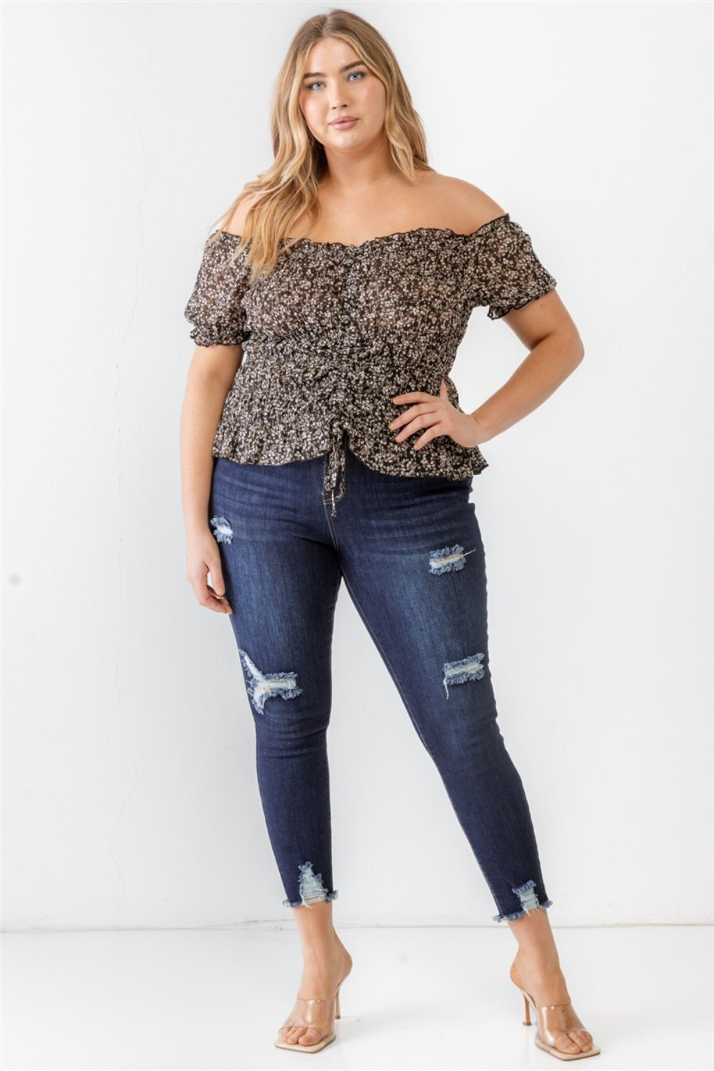 Wearing the Zenobia Plus Size Frill Ruched Off-Shoulder Short Sleeve Blouse and ripped jeans, a person with long hair poses against a plain white background.