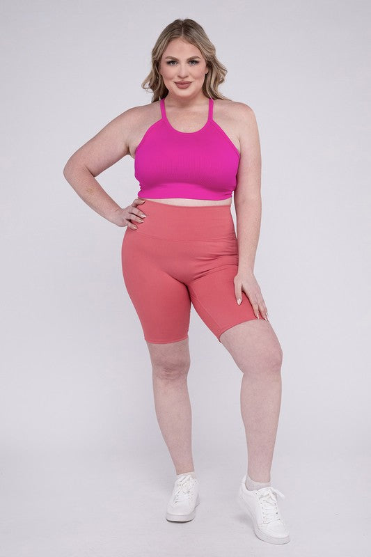 Against a plain background, a person showcases the Plus Athletic High Rise Biker Shorts in coral, crafted from high-quality athletic fabric and paired with a pink top.