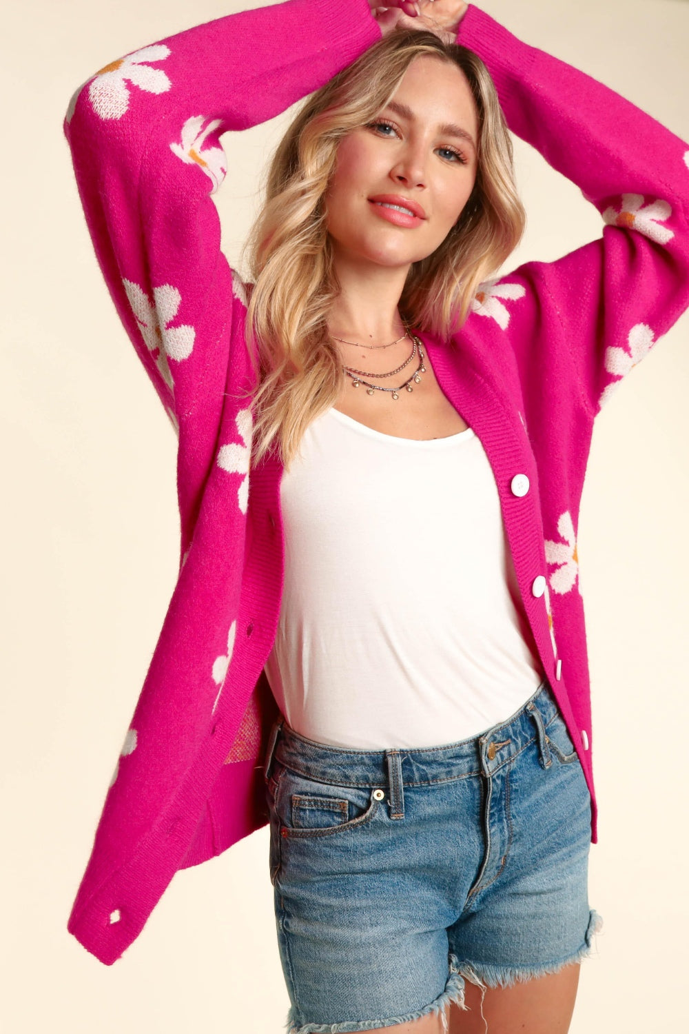 A person with long hair wears a white top under the Haptics Full Size Daisy Floral Button Down Long Sleeve Cardigan, paired with blue denim shorts.