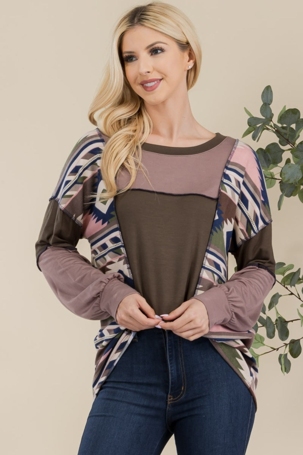 A woman with long blonde hair is wearing the Celeste Full Size Exposed Seam Printed Color Block T-Shirt and dark jeans, standing in front of a neutral background.