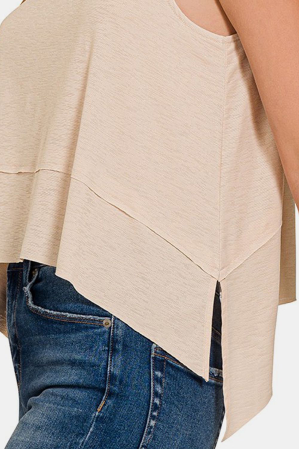 A woman with long, light brown hair wears a versatile piece: the Zenana Exposed Seam Slit Round Neck Tank in beige paired with blue jeans, standing against a plain background.