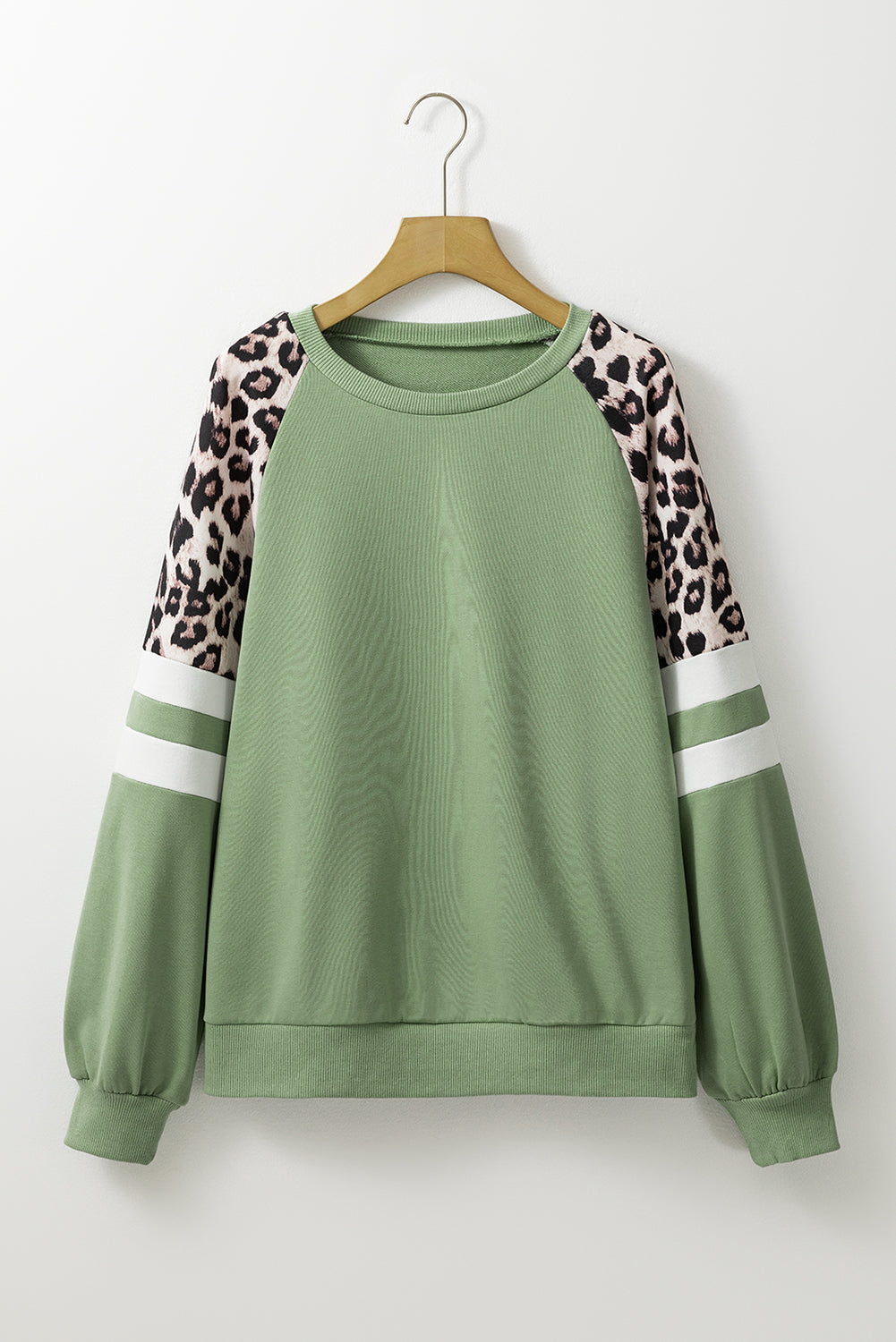 A person wearing a Grass Green Leopard Print Colorblock Raglan Sleeve Sweatshirt stands in front of a brick wall.
