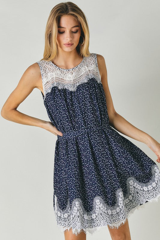 A woman wearing the Printed Sleeveless Lace Trim Mini Dress is seated against a light background.