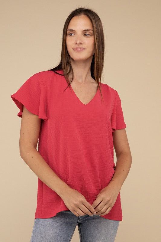 A woman with long straight hair models the Woven Airflow Flutter Sleeve Top in green, matched with light blue jeans, as she poses with her hands in her pockets against a plain beige background.