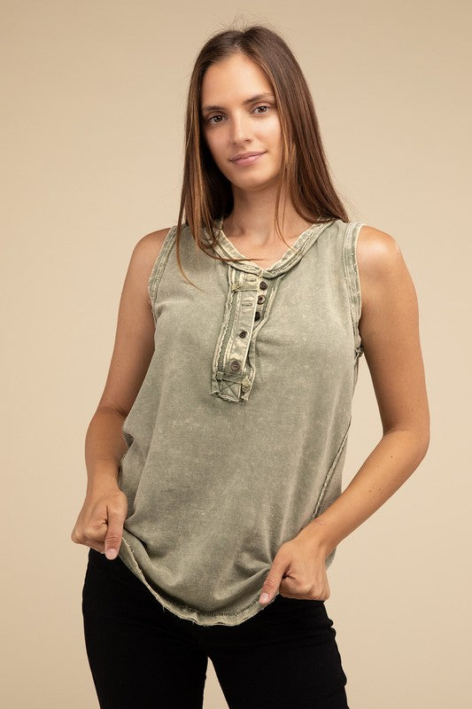 A woman with long brown hair is wearing the Washed Half-Button Raw Edge Sleeveless Henley Top in green and black pants, standing against a beige background.