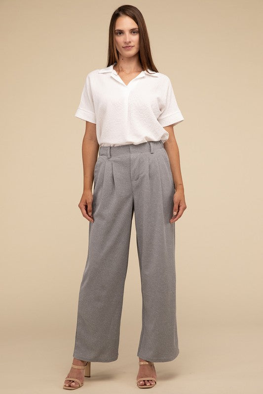 A woman stands against a beige background, highlighting her chic ensemble with a tailored fit. She wears a white short-sleeve shirt paired with versatile pink Waffle Trouser Pants, hands casually in pockets, complemented by stylish strappy sandals.