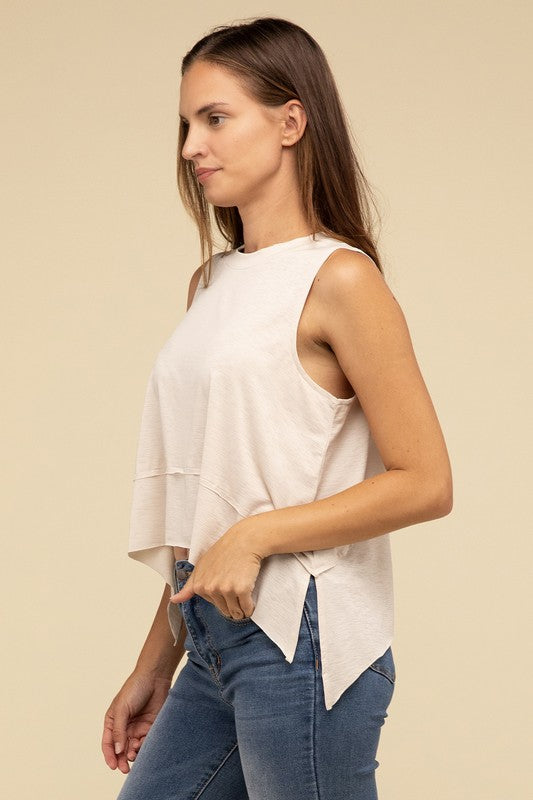 Wearing the Shark Bite Side Slit Short Sleeveless Top in maroon paired with white pants, a model is set against a beige background, exemplifying an effortlessly chic and casual wardrobe.