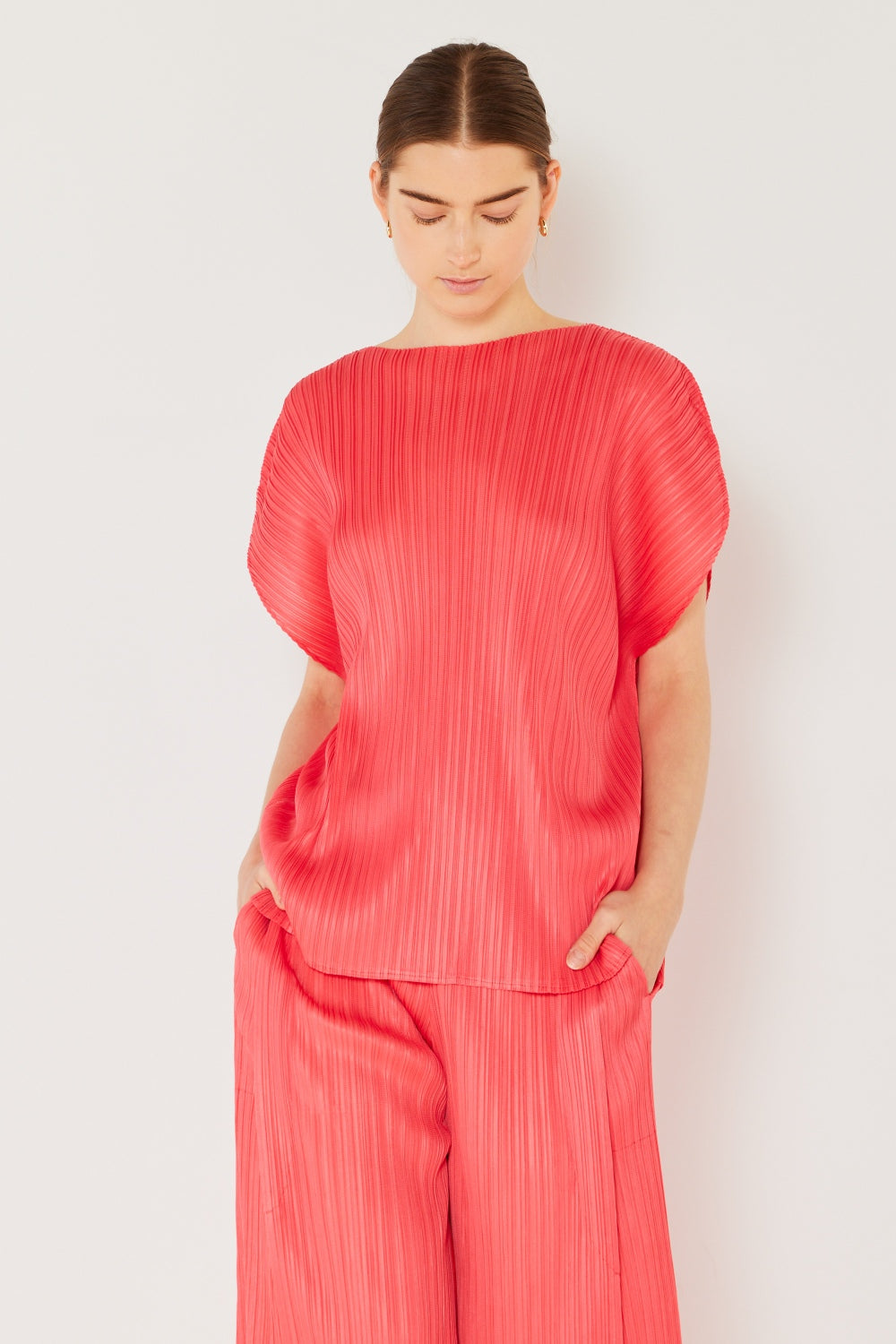 A person wearing the Marina West Swim Rib Pleated Oversized Dolman Sleeve Top in a fashionable light blue shade, paired with a brown belt and black skirt, stands against a plain background.