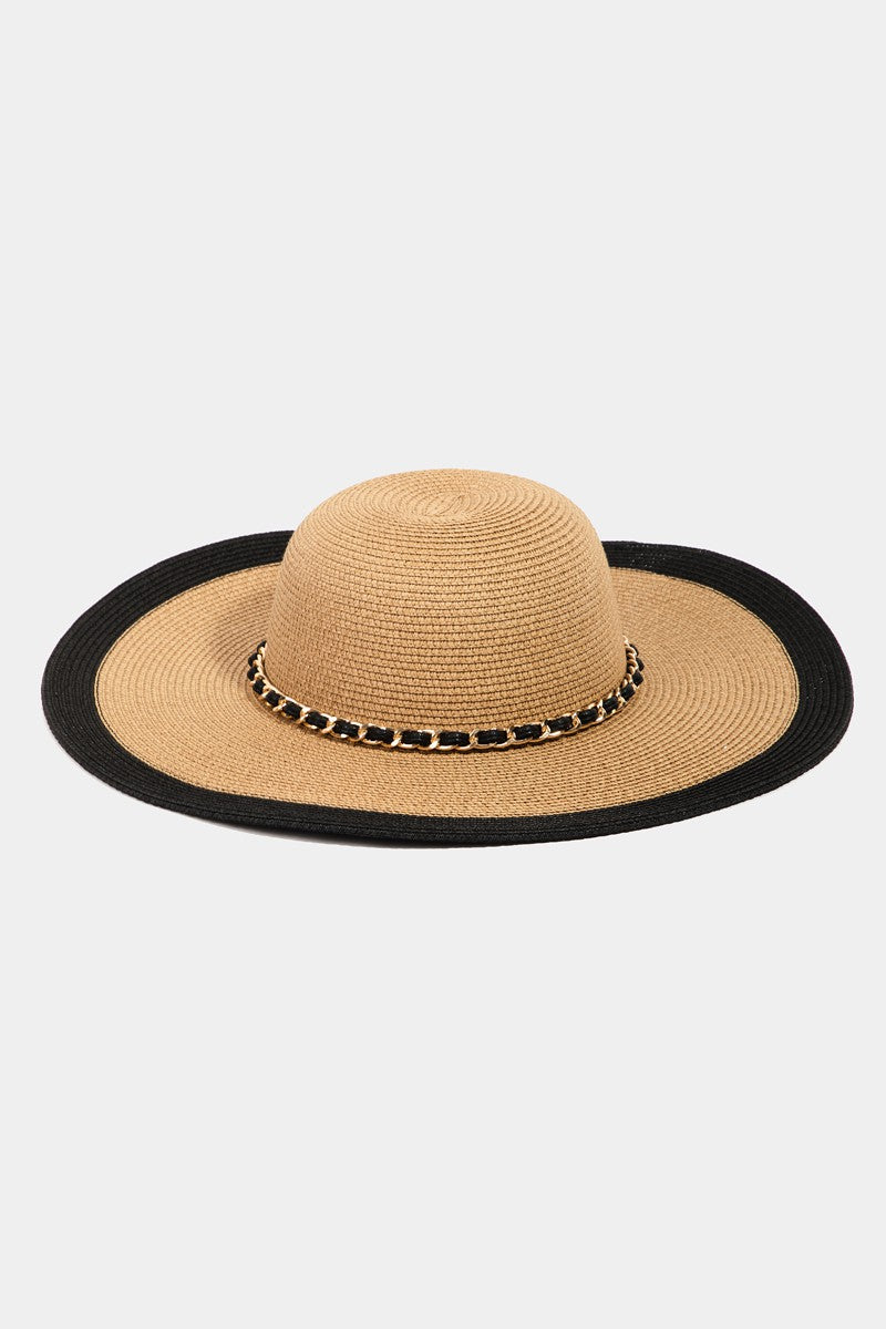 The Fame Chain Black Trim Straw Hat showcases a chic chain detail around its base, providing both elegance and sun protection with its wide brim.