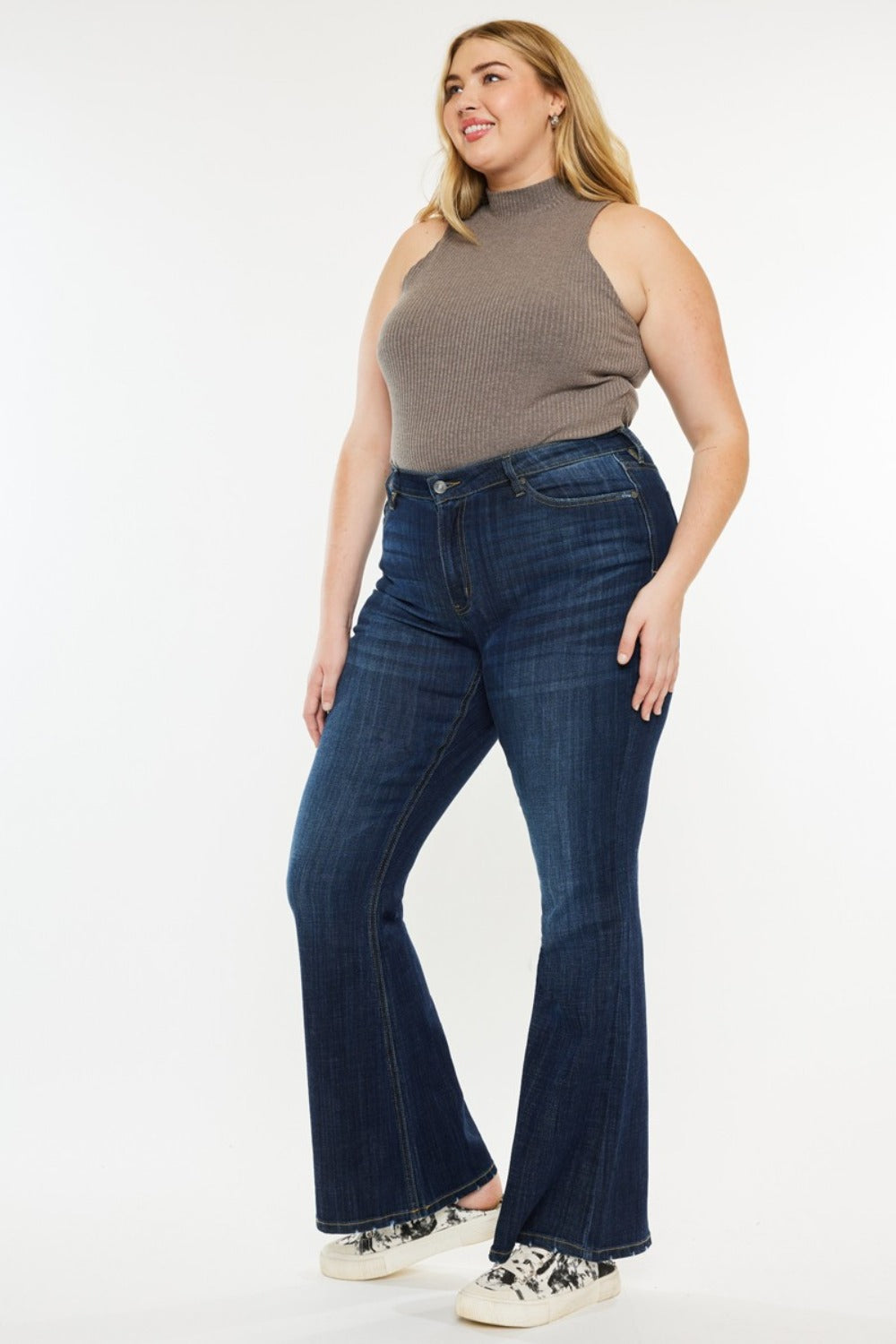 A person poses in a sleeveless brown top, Kancan Full Size Mid Rise Flare Jeans, and sneakers against a plain white background.