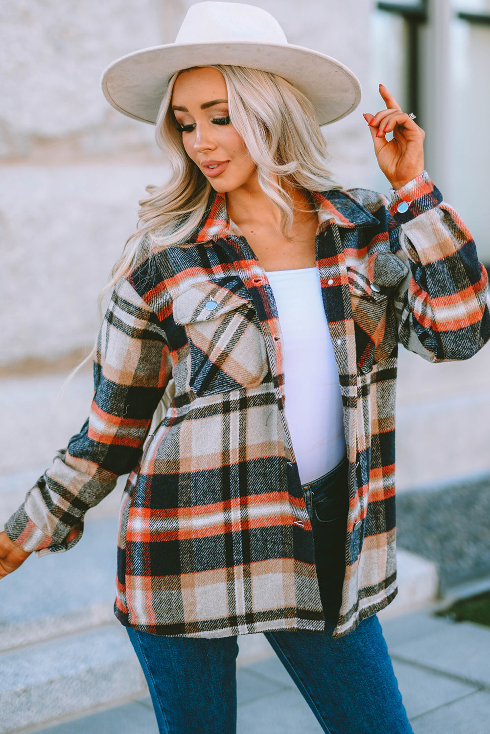 A person wearing a Brown Plaid Button Up Long Sleeve Flannel Shacket layered over a white top with ripped jeans and holding a brown handbag stands against a textured gray wall.