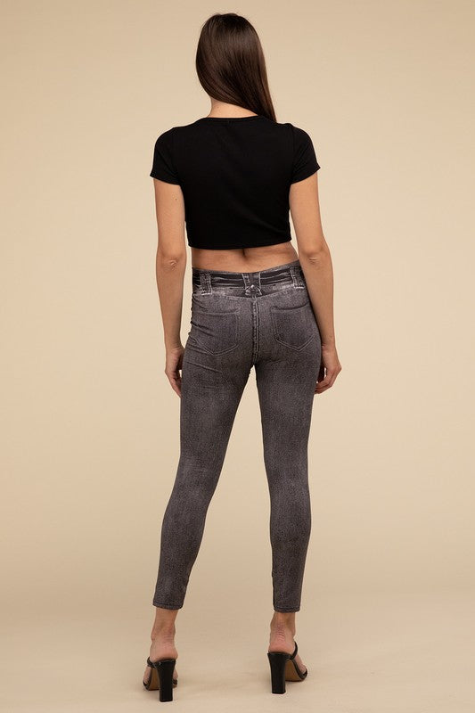 A person wearing Denim Leggings in a high-waisted black design and paired with black heels poses against a plain beige background, highlighting the sleek, stretchy fit.