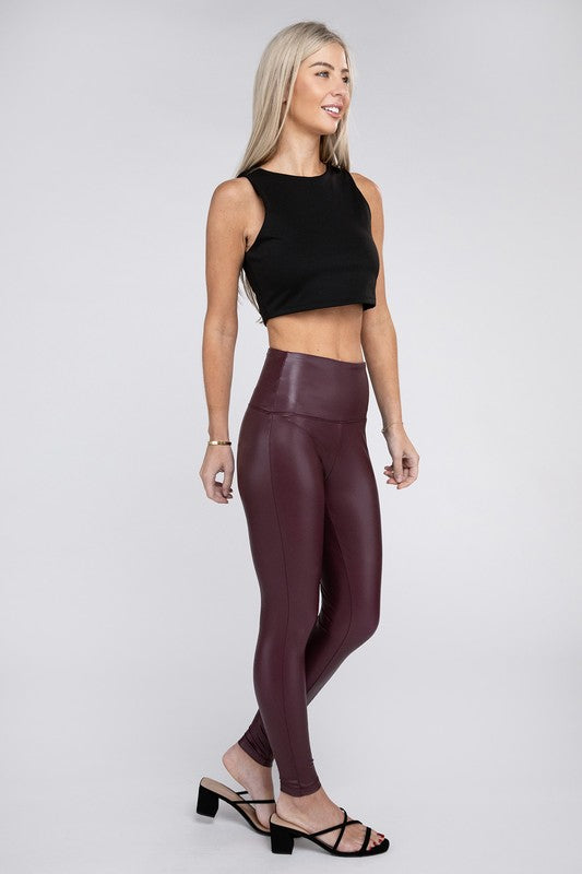 A woman stands confidently wearing a black sleeveless crop top, High Rise Faux Leather Leggings in maroon, and black strappy heels. She has long, straight hair and a neutral background, exuding a sporty and edgy look.