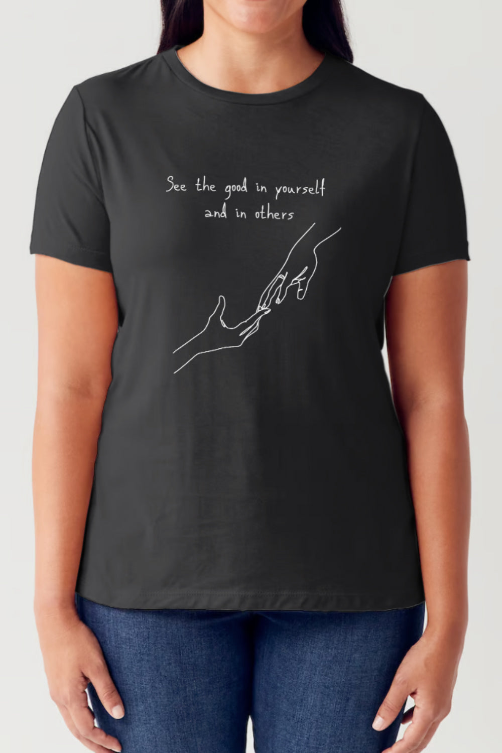 A person is wearing a Simply Love Full Size Slogan Graphic Short Sleeve Tubular T-Shirt, featuring a minimalist design of two hands reaching for each other. The text reads: "See the good in yourself and in others," delivering a positive message to all who see it.