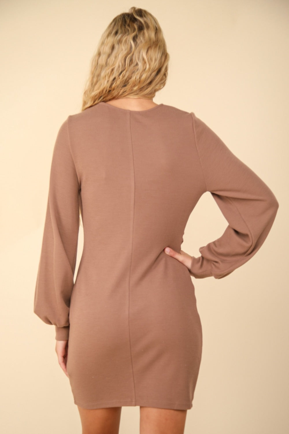 A person with long blonde hair is wearing the VERY J Ruched Detail Bodycon Mini Dress, which features a figure-hugging silhouette. They stand in front of a plain, beige background, effortlessly blending elegance and simplicity for special occasions.