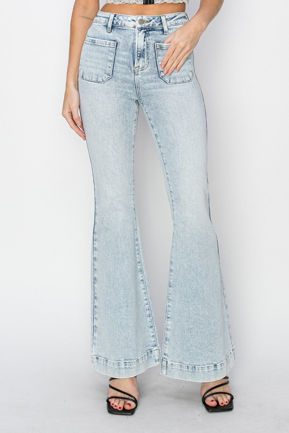 A person wearing Risen Full Size High Rise Front Patch Pocket Flare Jeans in a light wash, paired with black strappy sandals, stands against a white background.
