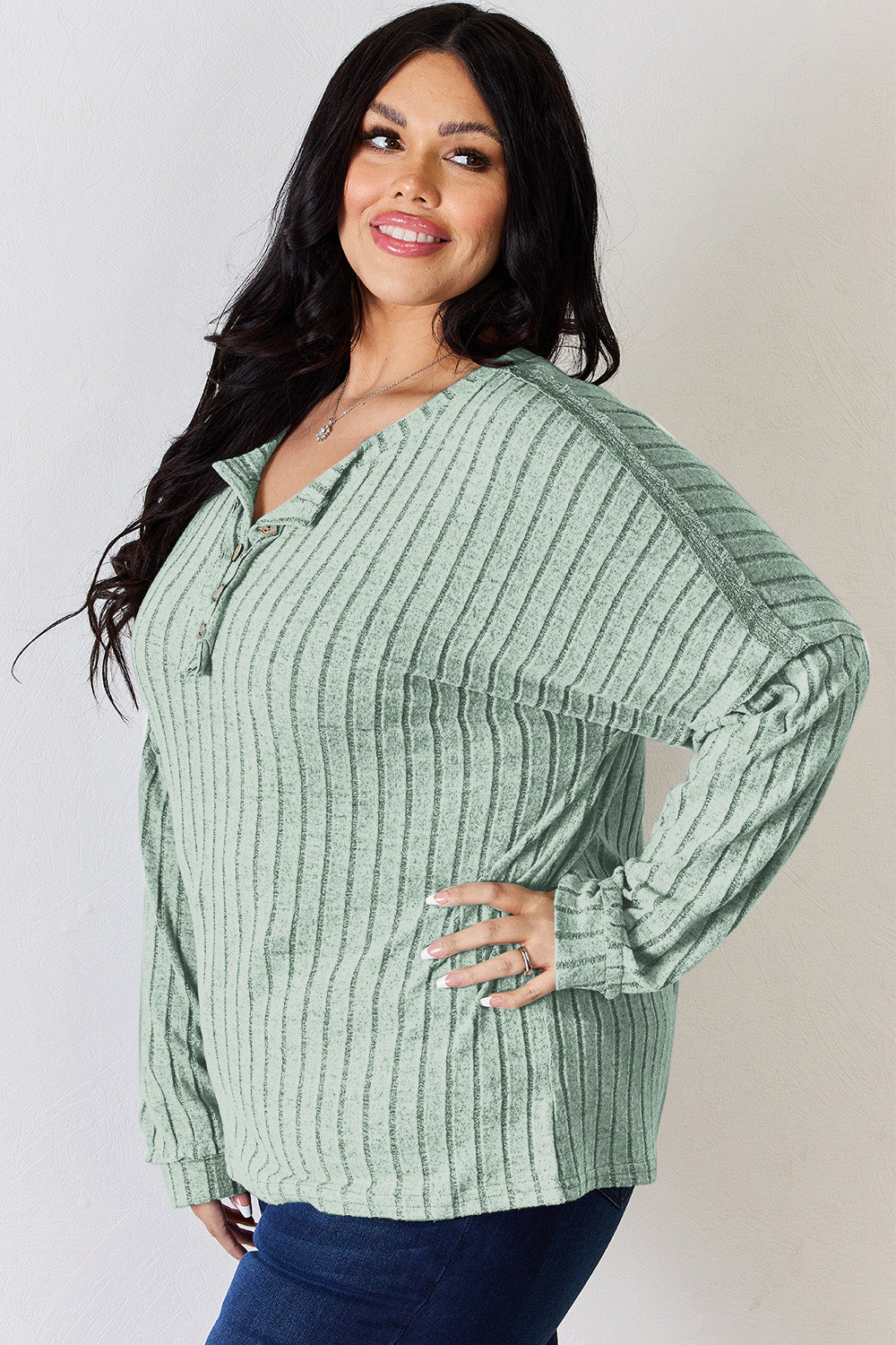 A woman with long, wavy blonde hair wears a slightly stretchy, textured Basic Bae Full Size Ribbed Half Button Long Sleeve T-Shirt in pink, standing against a neutral backdrop.