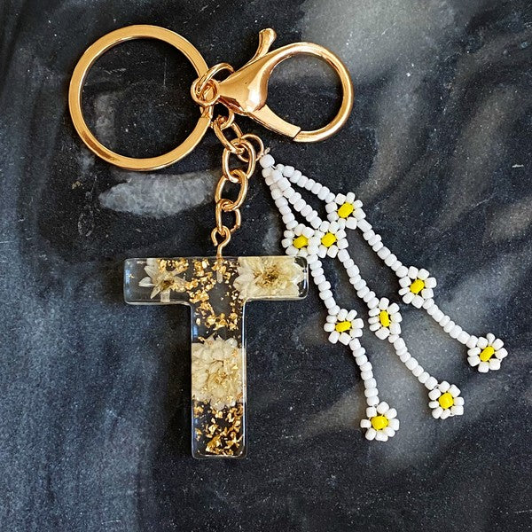 Baby Daisy Initial Key Chain alphabet keychains with real daisy flowers and gold flakes on a marble surface.