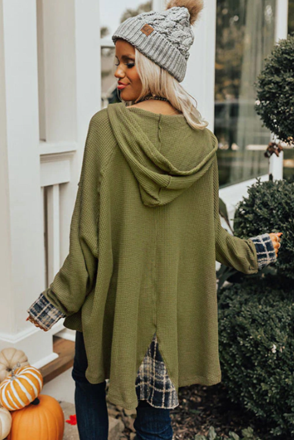 A person wearing a grey beanie, the Green Flowy Plaid Accent Waffle Knit Henley Hoodie, and a plaid shirt is standing outside next to a pumpkin and greenery.