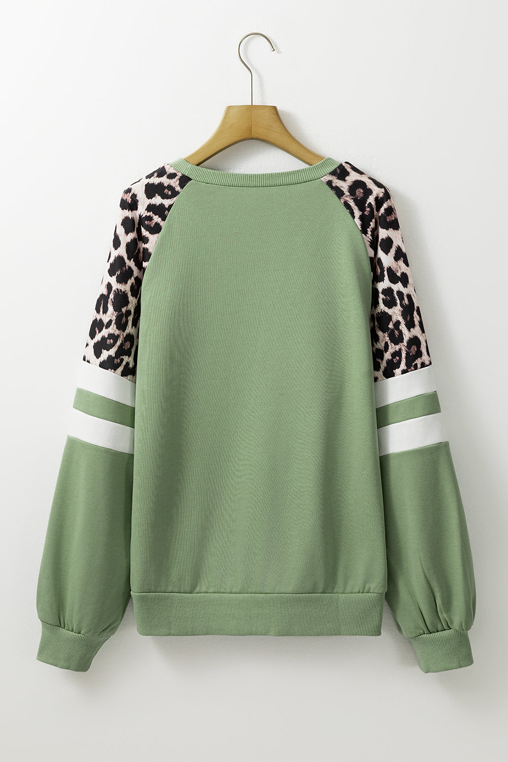 A person wearing a Grass Green Leopard Print Colorblock Raglan Sleeve Sweatshirt stands in front of a brick wall.