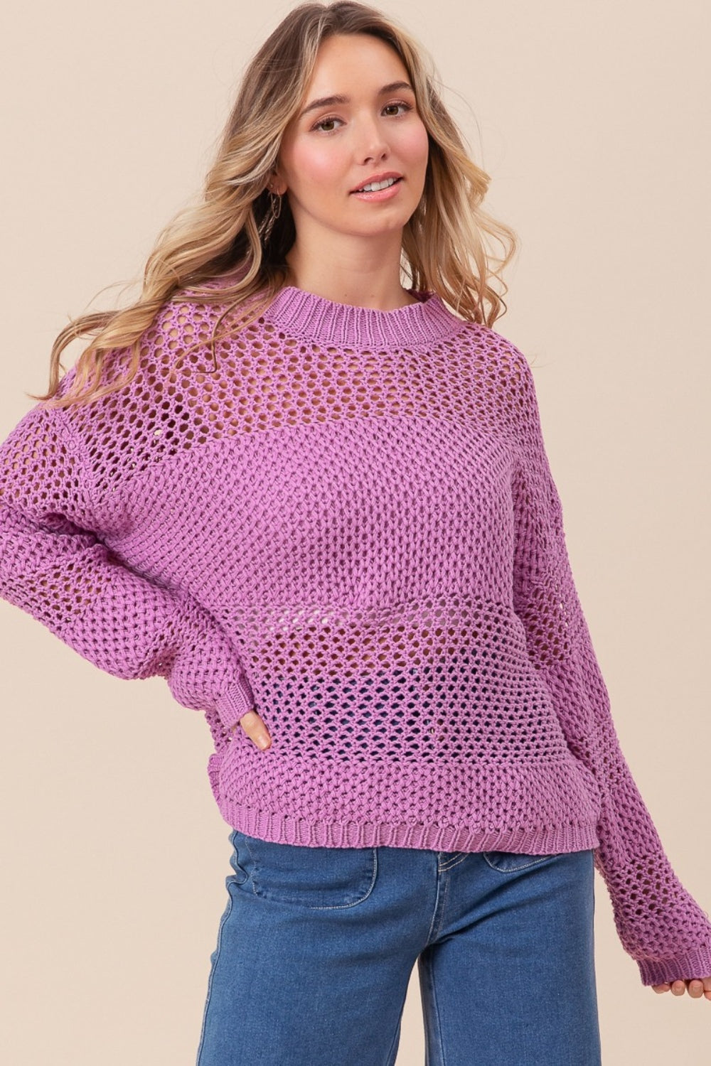 Wearing the BiBi Openwork Long Sleeve Knit Top in purple and blue jeans, a person smiles slightly while gazing to the side, exuding a fashion-forward vibe.