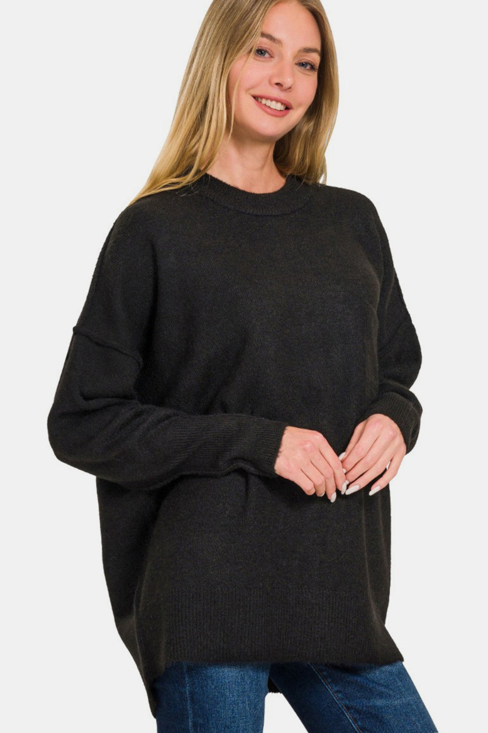 A person wearing the Zenana High-Low Hem Drop Shoulder Sweater, paired with jeans, poses elegantly against a plain background.