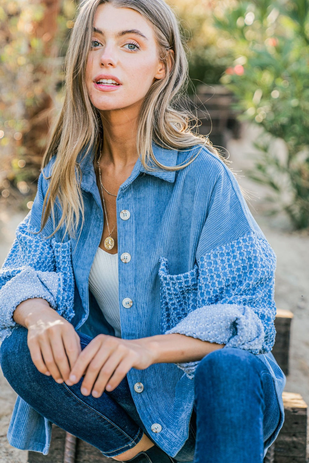 A woman stands outdoors wearing the And The Why Button Down Corduroy Contrast Texture Long Sleeve Shacket over a white top and blue jeans. She has long hair and wears a belt with a prominent buckle.