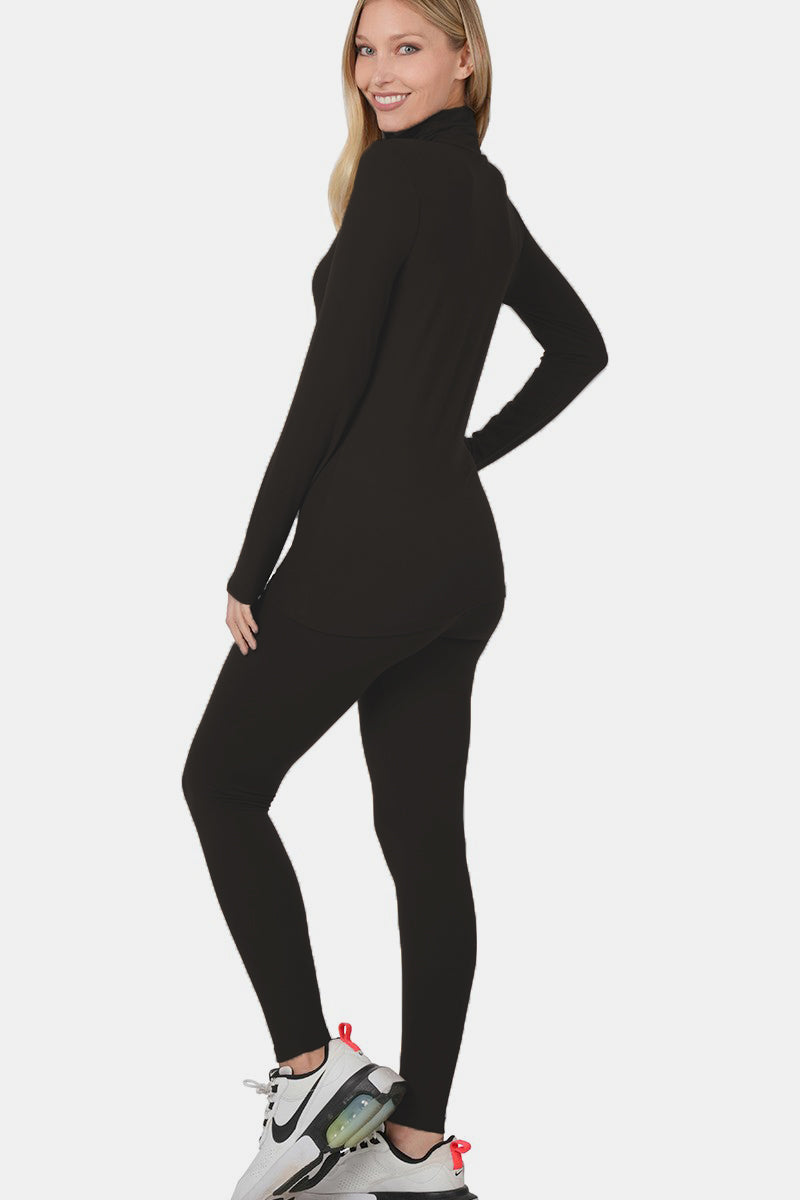 Wearing the Zenana Full Size Turtleneck Top and Leggings Lounge Set in sleek black, along with clean white sneakers, a person stands against a pristine white background.