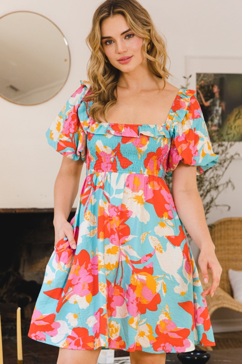 A woman wearing an ODDI Printed Smocked Puff Sleeve Mini Dress poses in a room decorated with a mirror and framed art on the wall.