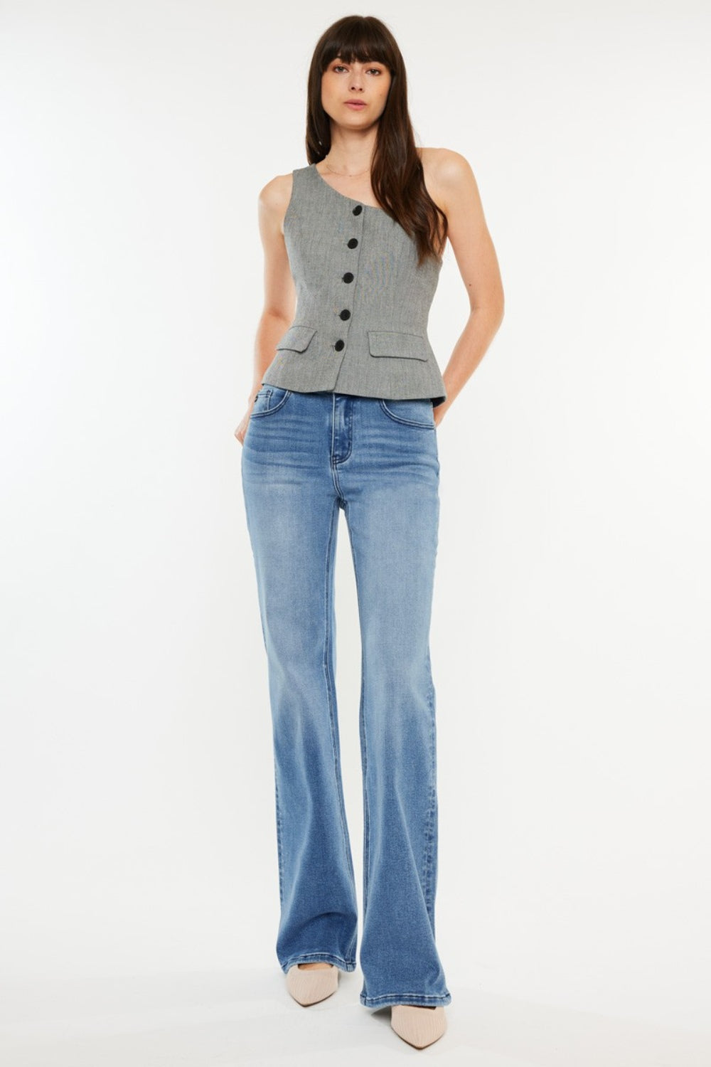 A person stands wearing a sleeveless, buttoned top paired with Kancan Ultra High Rise Cat's Whiskers Jeans. They have long, dark hair and are standing against a plain white background.