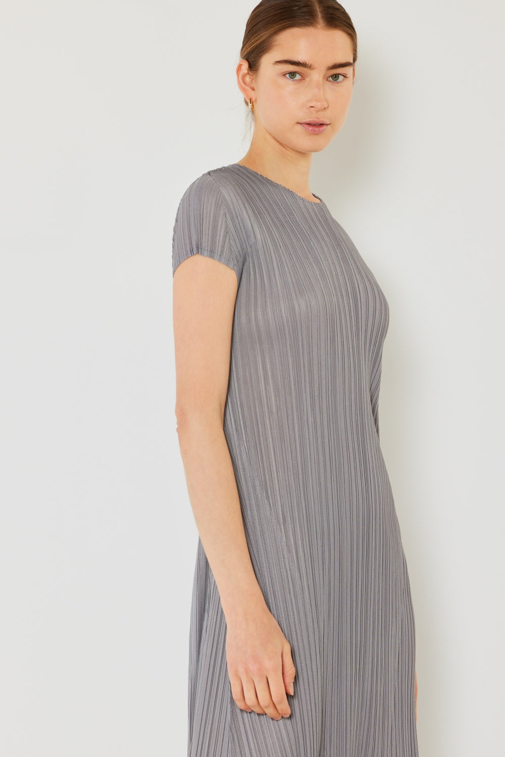 A person stands against a light wall, wearing an elegant Marina West Swim Pleated Cap Sleeve A-Line Dress in black and white sandals.