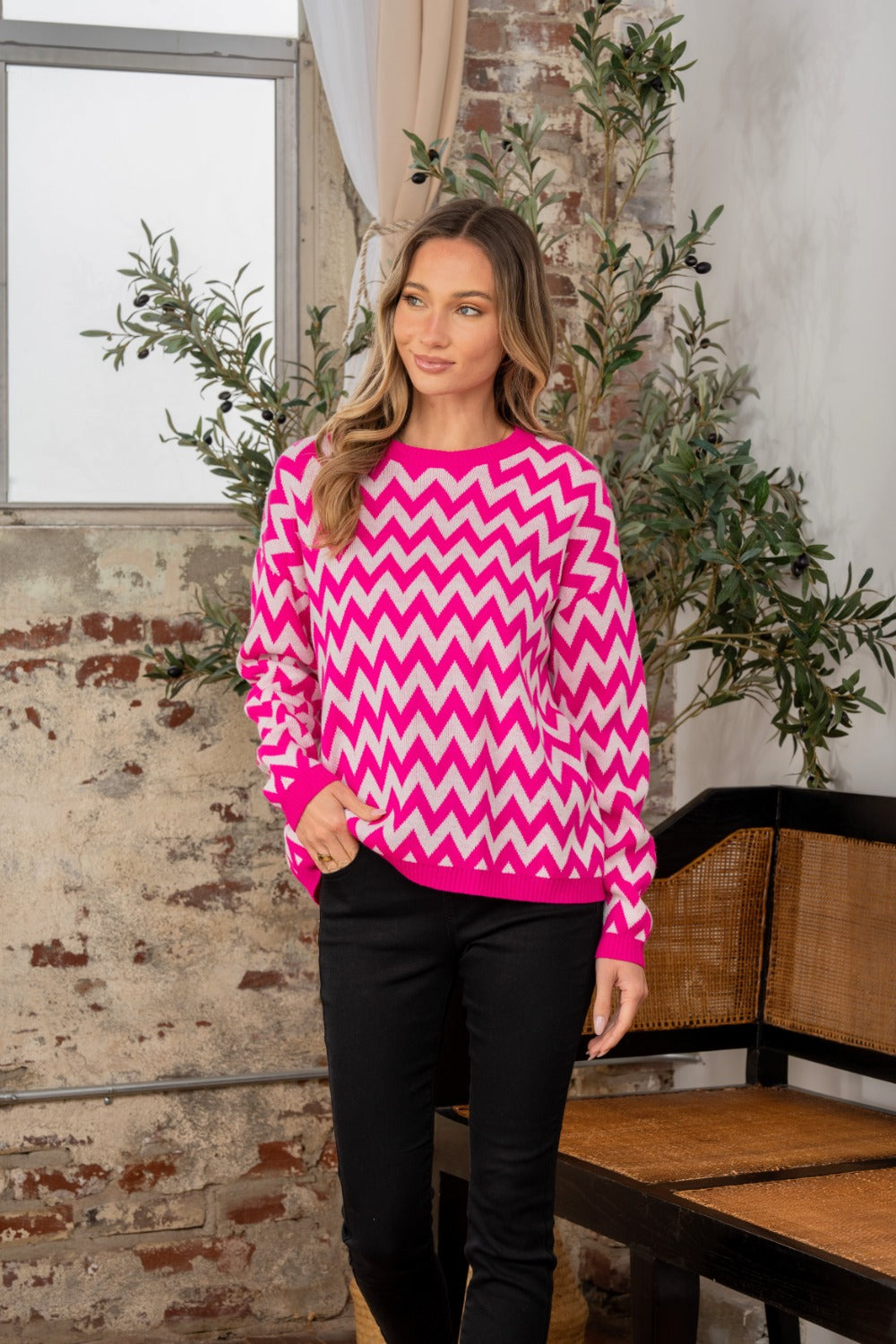 A person wearing the Sew In Love Full Size Wave Stripe Contrast Long Sleeve Sweater stands indoors near a potted plant and a brick wall.