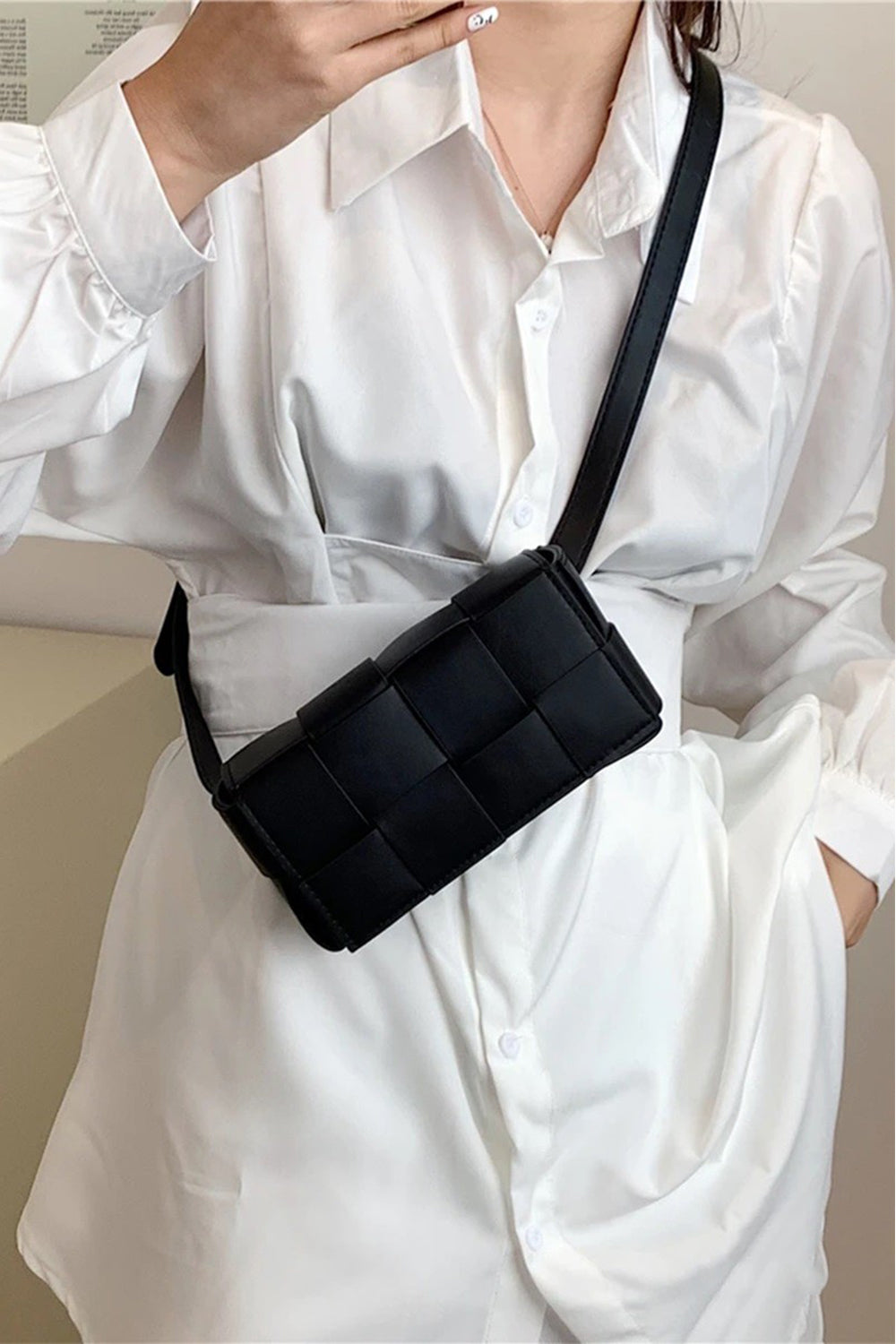 Person wearing a white button-up shirt and holding a black Zenana Vegan Leather Woven Crossbody Bag.